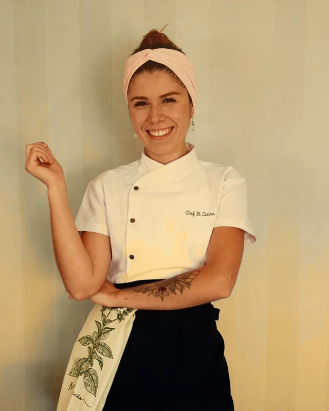 Chef Bí Cunha sorrindo, de dólmã branco e avental